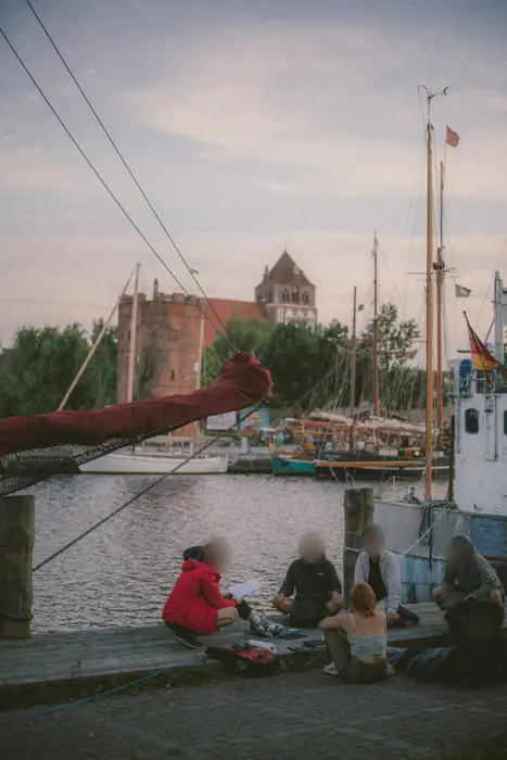 Eine Gruppe sitzt am Kai vor einem Boot, dahinter die Stadt