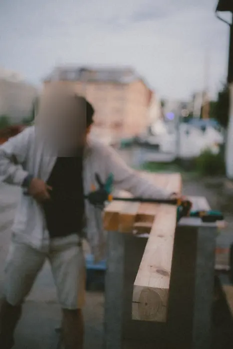 Zwei Menschen tragen einen Holzbalken über das Werftgelände